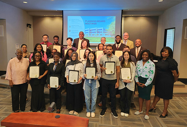 Group of young people holding certificates in the center of a room with supervisors on the outer edges of the group.